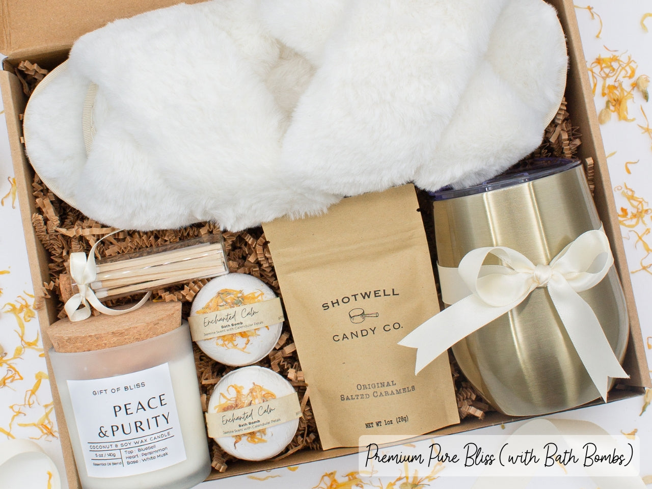 Luxury gift box for her. Featuring a stainless steel tumbler, an aromatherapy candle with matches, luxury bath bombs, plush open-toe slippers, and gourmet caramel treats. All items are beautifully arranged for a pampering experience.