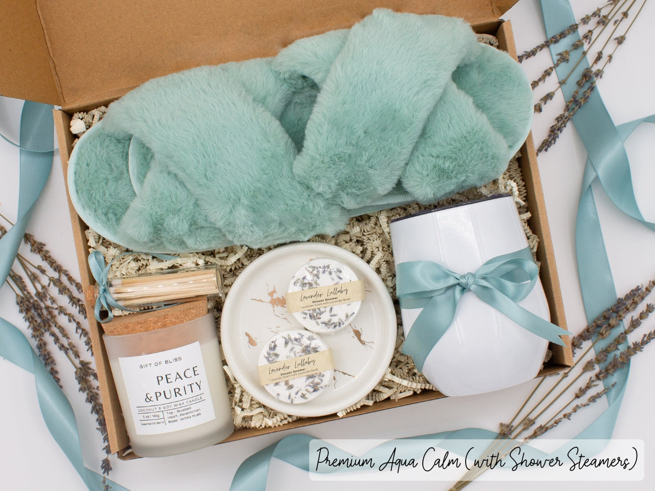 Luxury gift box for her. Featuring a stainless steel tumbler, an aromatherapy candle with matches, aromatic shower steamers, sleek ceramic dish, and plush open-toe slippers. All items are beautifully arranged for a pampering experience.