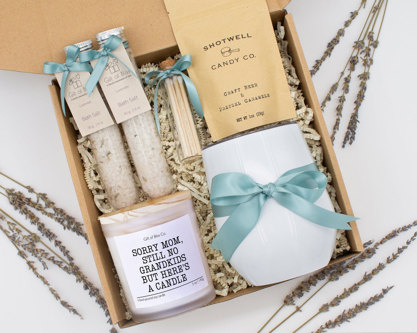 A luxury spa gift box for mom featuring a stainless steel tumbler, an aromatherapy candle with matches, therapeutic bath salt, and gourmet caramel treats. All items are beautifully arranged for a pampering experience.
