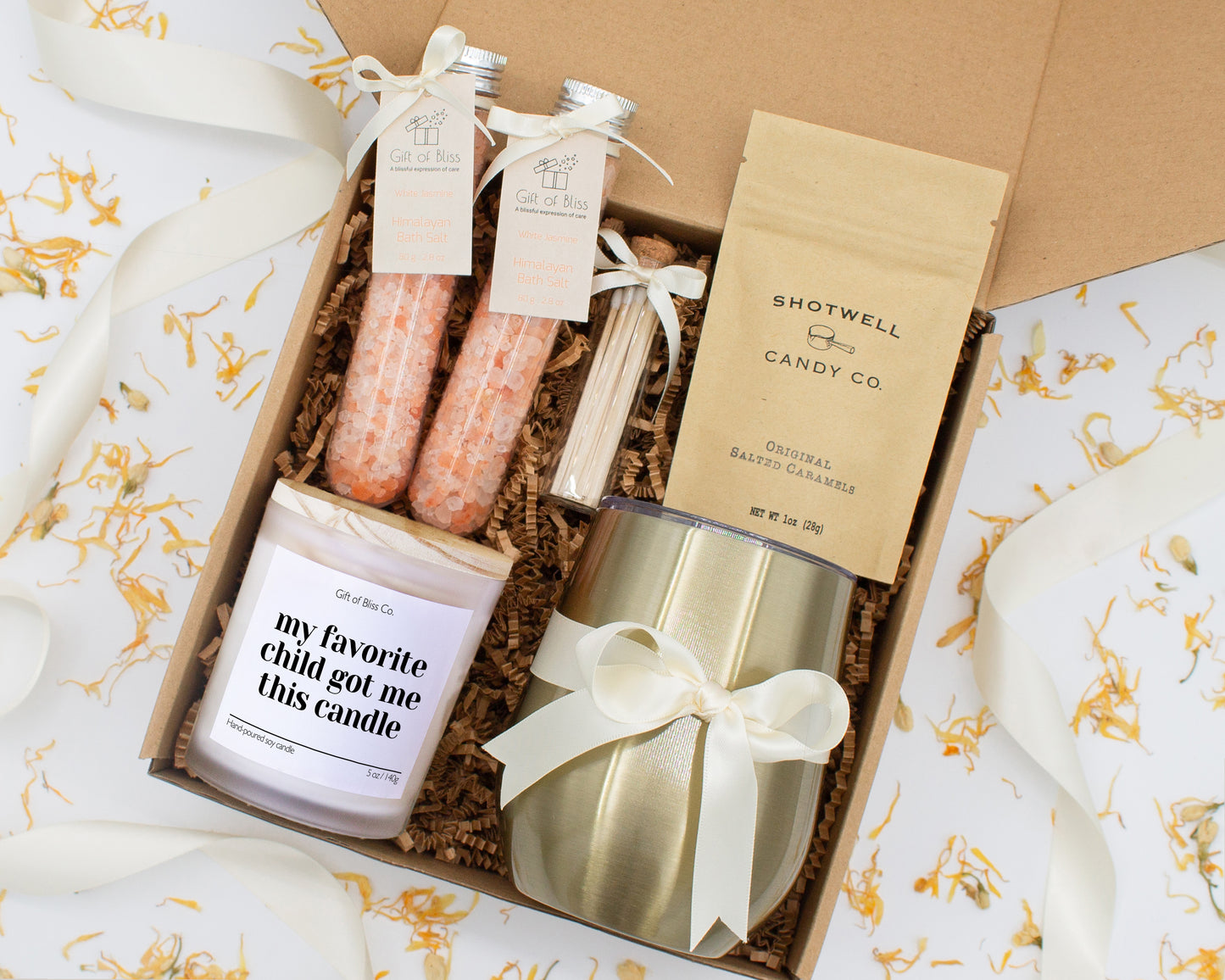A luxury spa gift box for mom featuring a stainless steel tumbler, an aromatherapy candle with matches, therapeutic bath salt, and gourmet caramel treats. All items are beautifully arranged for a pampering experience.