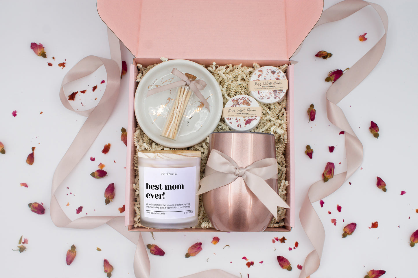 A luxury spa gift box for mom featuring a stainless steel tumbler, an aromatherapy candle with matches, therapeutic shower steamers, and gourmet caramel treats. All items are beautifully arranged for a pampering experience.