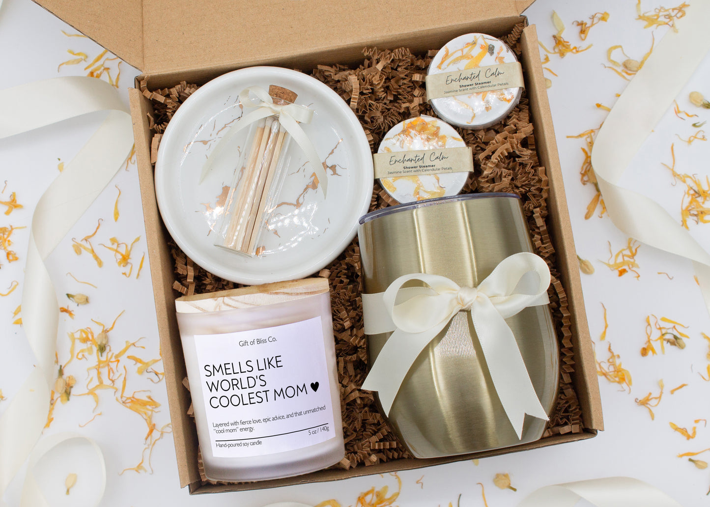 A luxury spa gift box for mom featuring a stainless steel tumbler, an aromatherapy candle with matches, therapeutic shower steamers, and gourmet caramel treats. All items are beautifully arranged for a pampering experience.