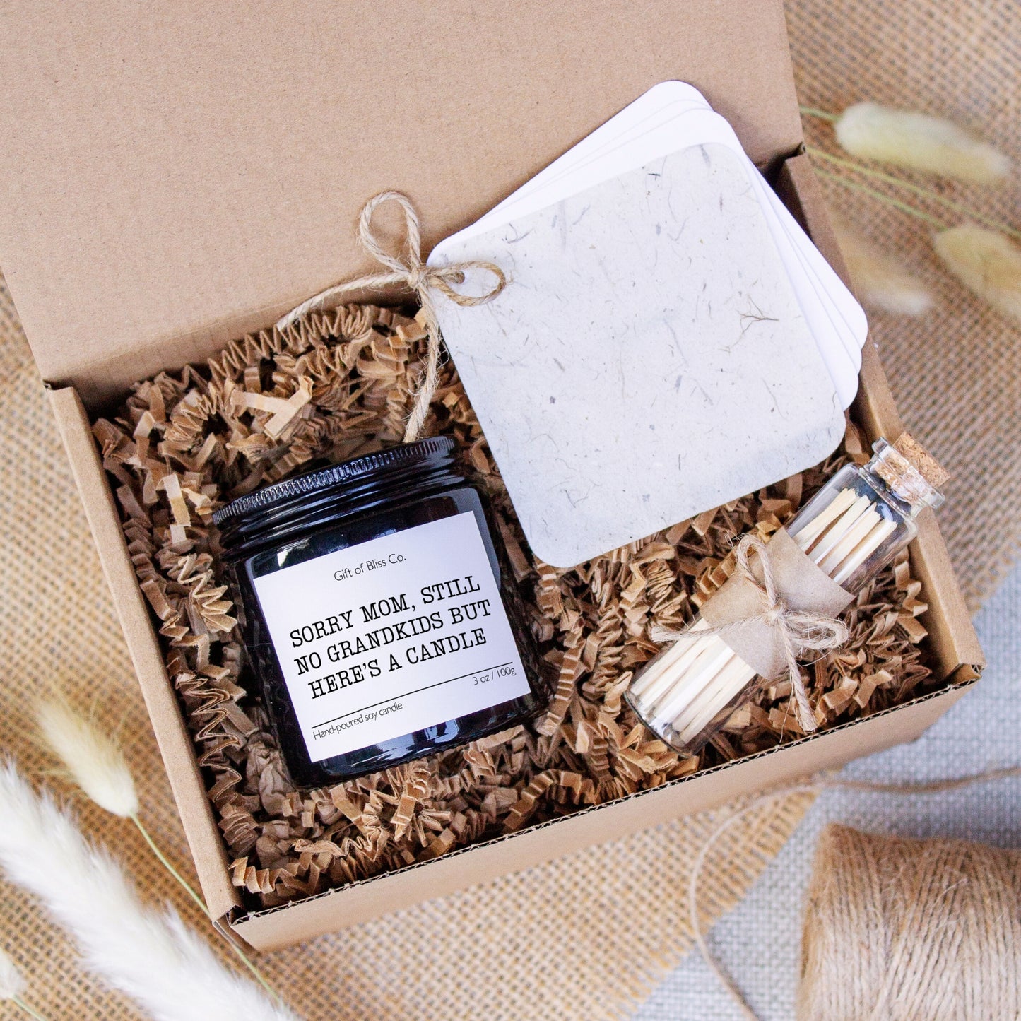 Candle gift box featuring a “Sorry mom, still no grandkids but here's a candle” soy candle, glass match jar, and a rustic-style personalized message booklet tied with jute twine. Arranged in a kraft box with crinkle paper filler and neutral tones, this cozy, witty, handcrafted gift is perfect for Mother’s Day or mom appreciation. A heartfelt and aesthetic set that combines warmth, functionality, and rustic charm.