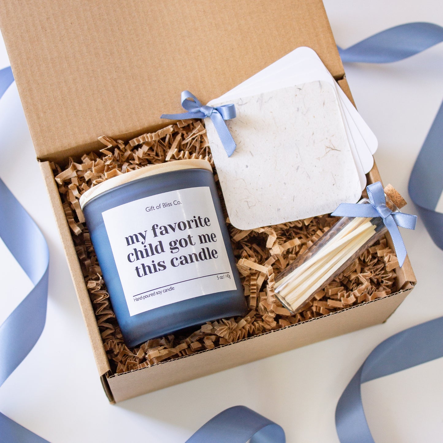 Candle gift box featuring a “My favorite child got me this candle” soy candle, glass match jar, and a personalized message booklet tied with blue ribbon. Arranged in a kraft box with crinkle paper filler and neutral tones, this cozy, elegant, handcrafted gift is perfect for Mother’s Day or mom appreciation. A heartfelt and aesthetic set that combines warmth, functionality, and luxury charm.