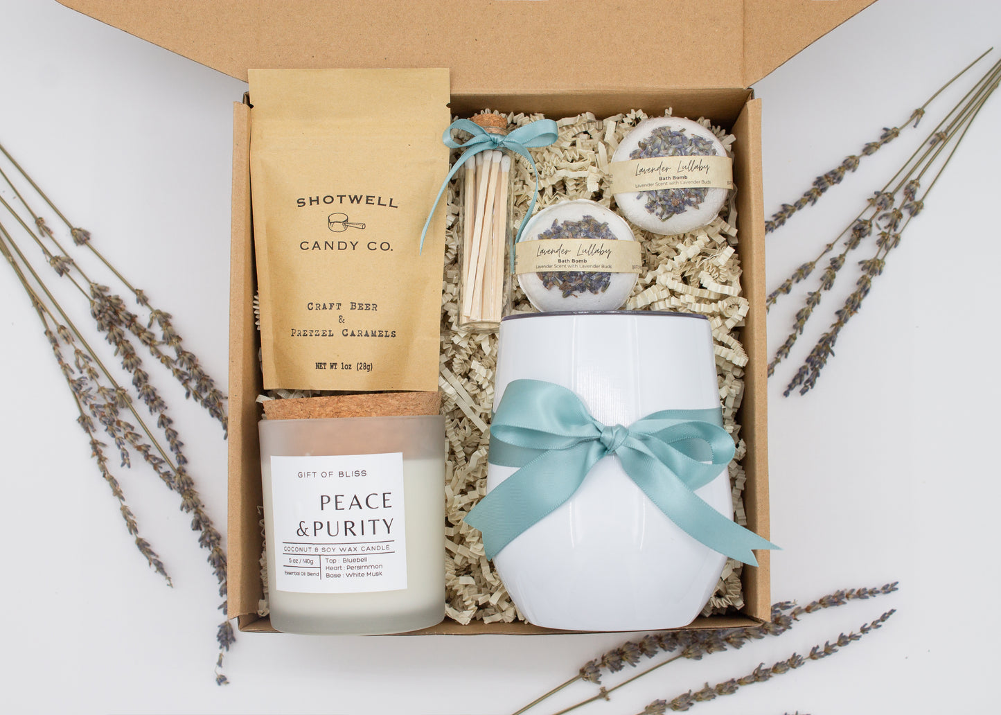 Luxury gift box for her. Featuring a stainless steel tumbler, an aromatherapy candle with matches, luxury bath bombs, and gourmet caramel treats. All items are beautifully arranged for a pampering experience.