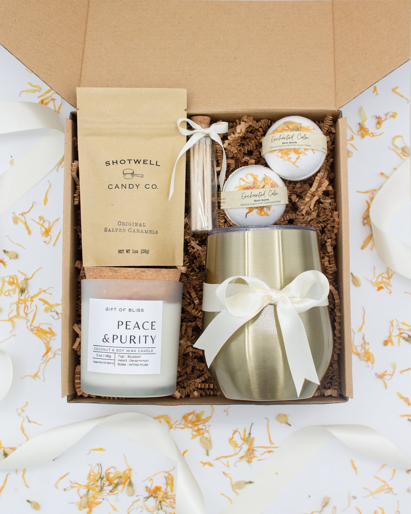 Luxury gift box for her. Featuring a stainless steel tumbler, an aromatherapy candle with matches, luxury bath bombs, and gourmet caramel treats. All items are beautifully arranged for a pampering experience.