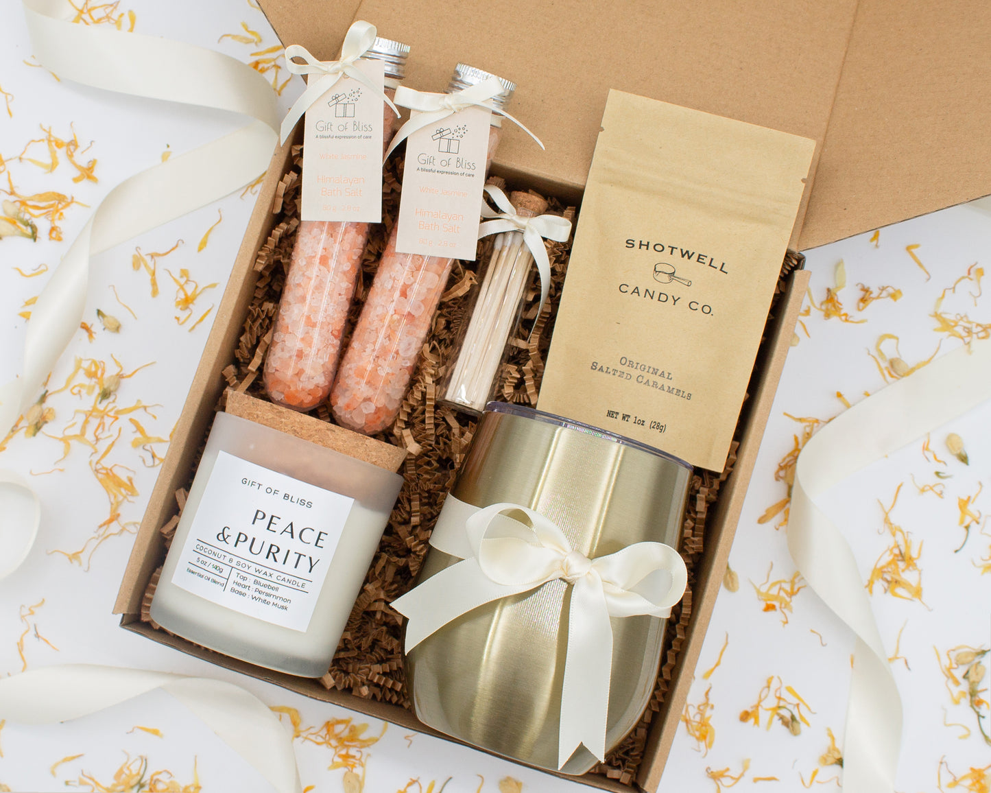 Luxury gift box for her. Featuring a stainless steel tumbler, an aromatherapy candle with matches, therapeutic bath salt, and gourmet caramel treats. All items are beautifully arranged for a pampering experience.