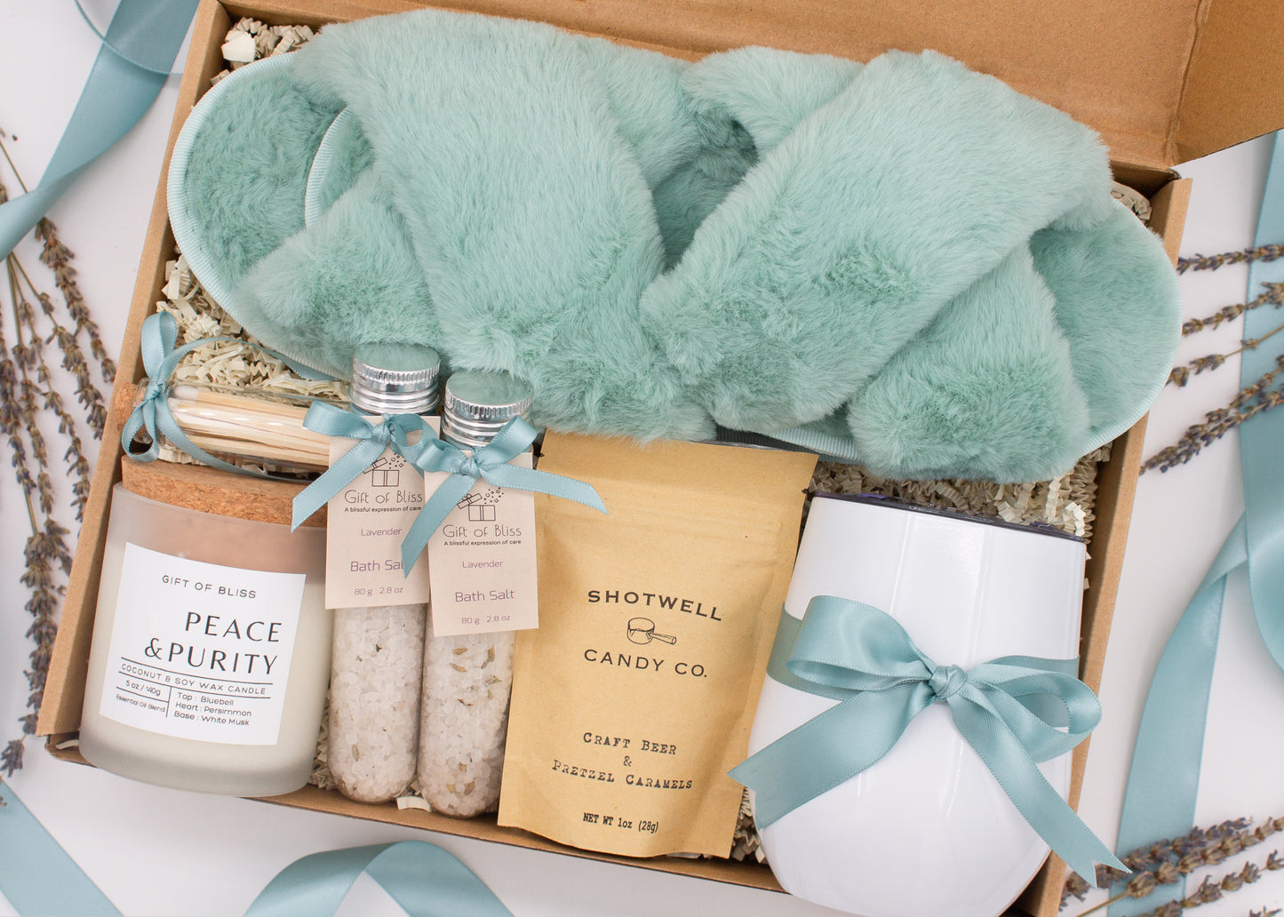 Luxury gift box for her. Featuring a stainless steel tumbler, an aromatherapy candle with matches, therapeutic bath salt, plush open-toe slippers, and gourmet caramel treats. All items are beautifully arranged for a pampering experience.