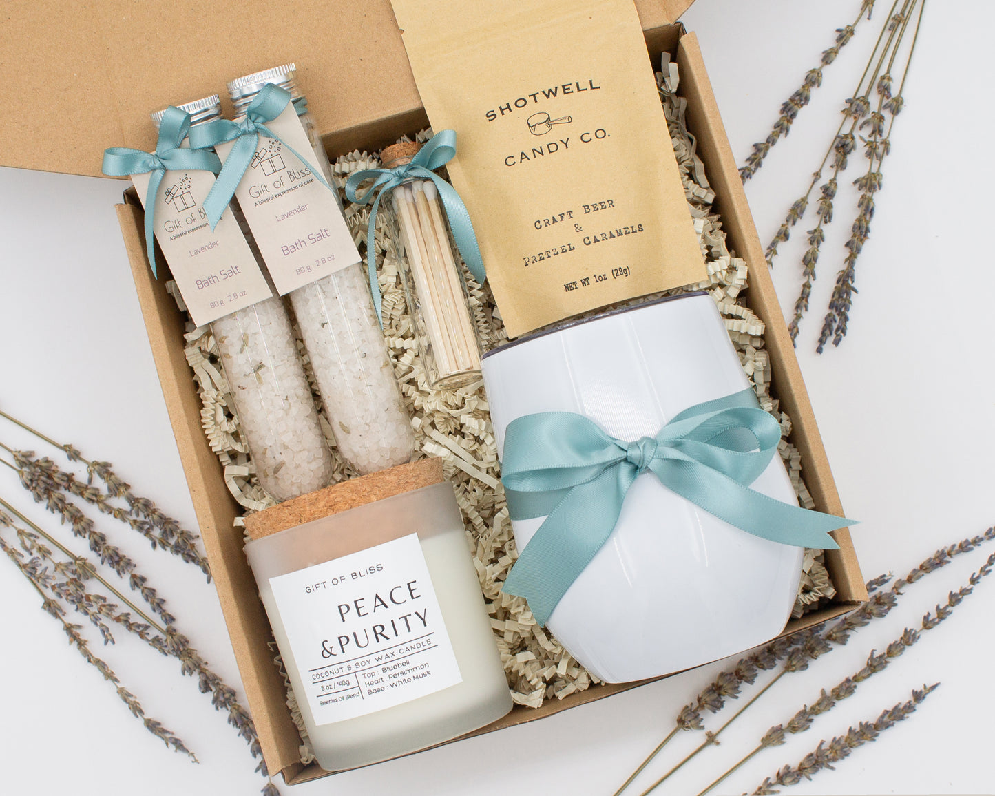Luxury gift box for her. Featuring a stainless steel tumbler, an aromatherapy candle with matches, therapeutic bath salt, and gourmet caramel treats. All items are beautifully arranged for a pampering experience.