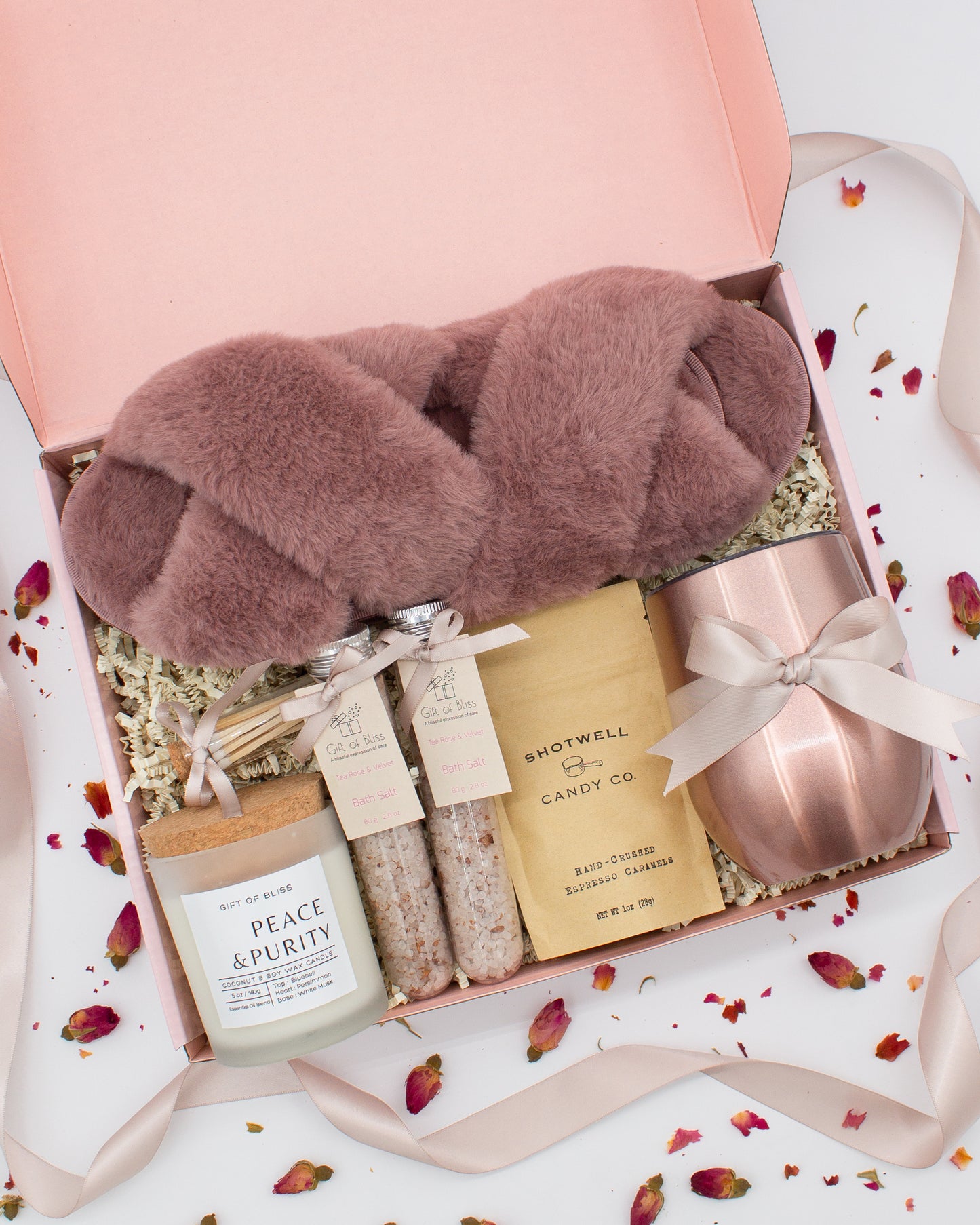 Luxury gift box for her. Featuring a stainless steel tumbler, an aromatherapy candle with matches, therapeutic bath salt, plush open-toe slippers, and gourmet caramel treats. All items are beautifully arranged for a pampering experience.