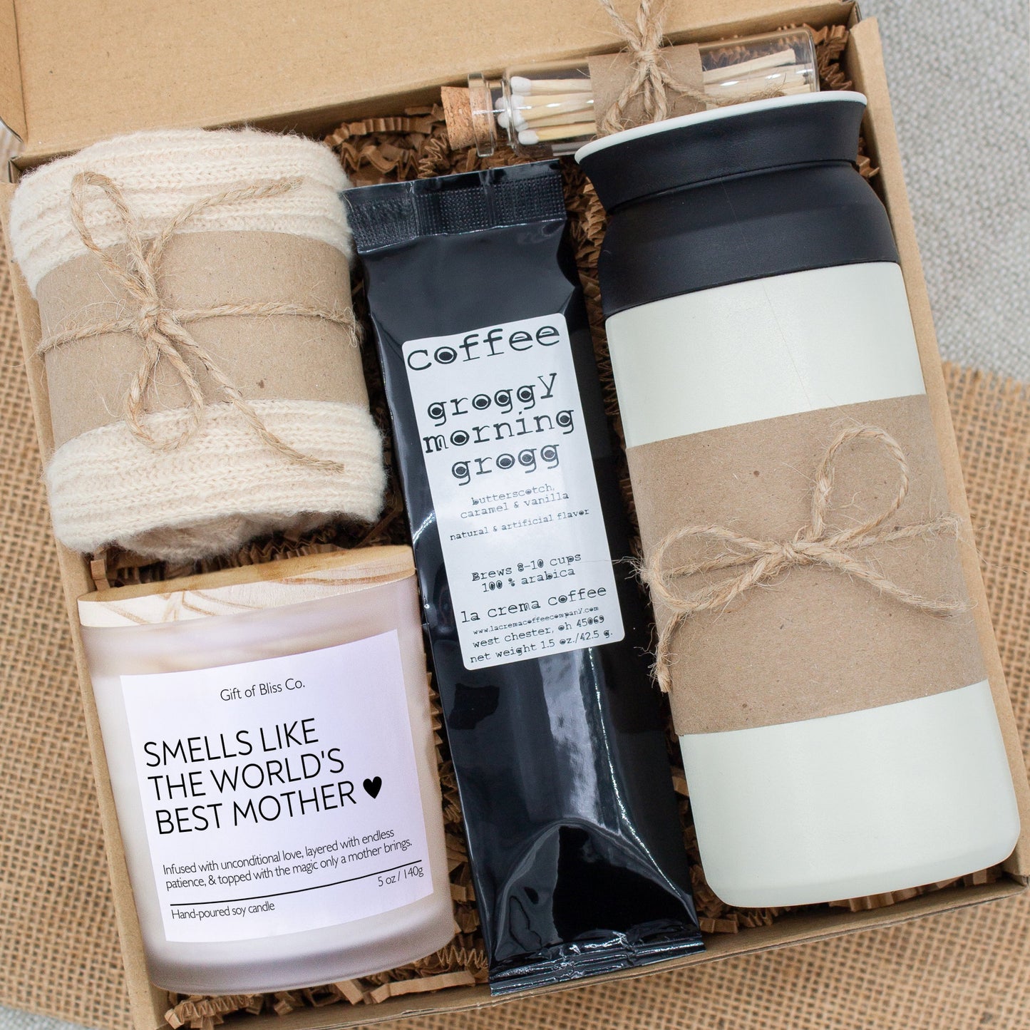 Rustic Retreat gift box in Basic Rustic Neutral theme, featuring a white 12oz stainless steel tumbler, “Smells like the world best mother" candle, safety match jar, mocha latte coffee, salted caramels, and cozy socks. All items are arranged in kraft paper with jute cord for a charming, earthy presentation. A thoughtful, cozy gift set ideal for Mother’s Day or self-care.