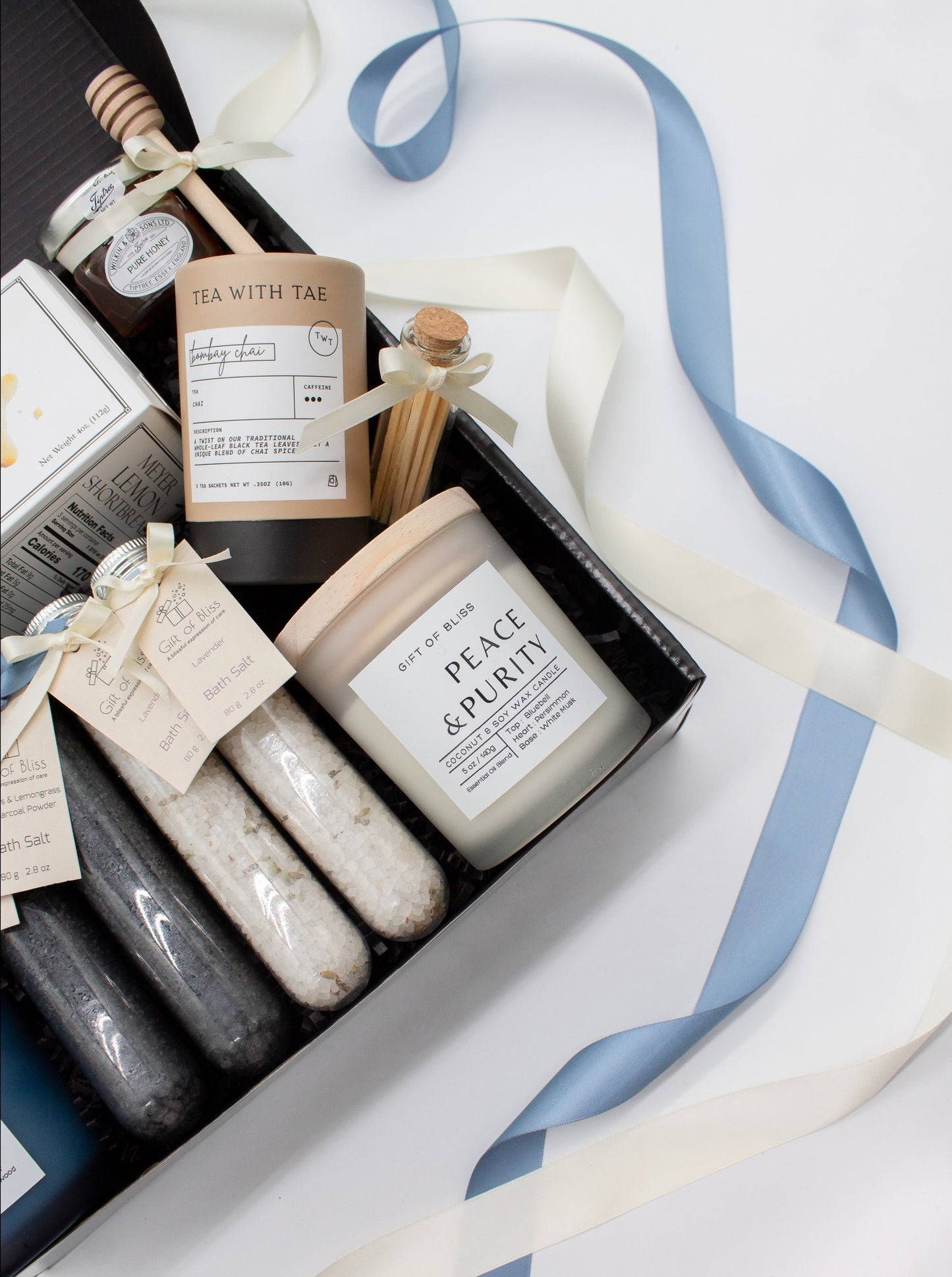 A spa gift box for two. Features shortbread cookies, 2 soothing tea blends, pure honey and wooden dipper, 2 aromatic candles, and 2 sets of bath salt. This elegantly curated box, ideal for couples, enhances shared moments of intimacy and relaxation.