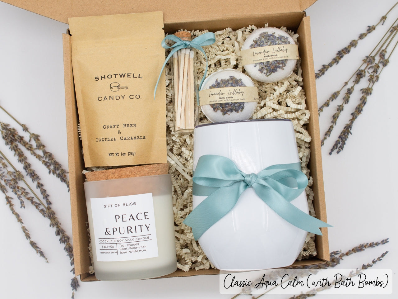 Luxury gift box for her. Featuring a stainless steel tumbler, an aromatherapy candle with matches, luxury bath bombs, and gourmet caramel treats. All items are beautifully arranged for a pampering experience.