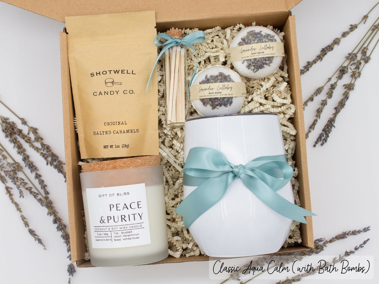 Luxury gift box for her. Featuring a stainless steel tumbler, an aromatherapy candle with matches, luxury bath bombs, and gourmet caramel treats. All items are beautifully arranged for a pampering experience.
