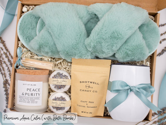 Luxury gift box for her. Featuring a stainless steel tumbler, an aromatherapy candle with matches, luxury bath bombs, plush open-toe slippers, and gourmet caramel treats. All items are beautifully arranged for a pampering experience.