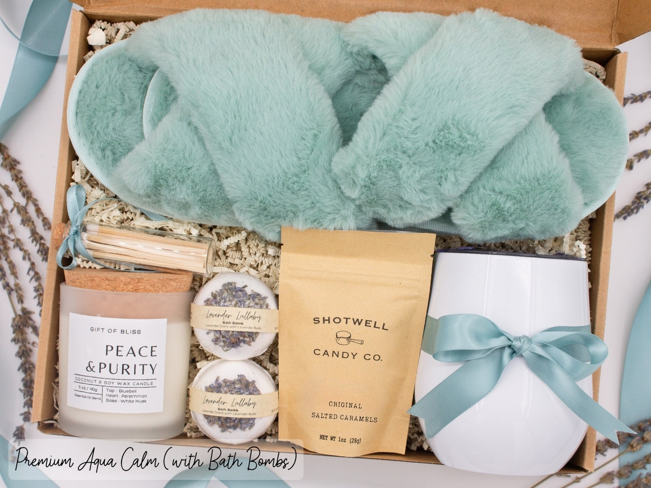 Luxury gift box for her. Featuring a stainless steel tumbler, an aromatherapy candle with matches, luxury bath bombs, plush open-toe slippers, and gourmet caramel treats. All items are beautifully arranged for a pampering experience.