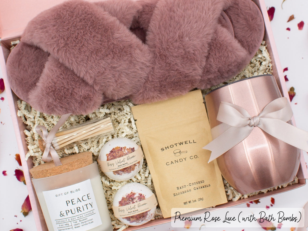 Luxury gift box for her. Featuring a stainless steel tumbler, an aromatherapy candle with matches, luxury bath bombs, plush open-toe slippers, and gourmet caramel treats. All items are beautifully arranged for a pampering experience.