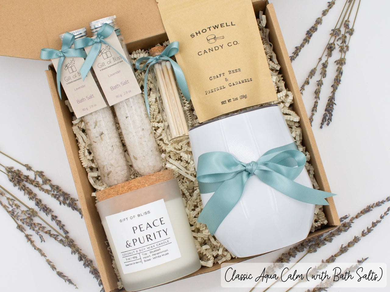 Luxury gift box for her. Featuring a stainless steel tumbler, an aromatherapy candle with matches, therapeutic bath salts, and gourmet caramel treats. All items are beautifully arranged for a pampering experience.a
