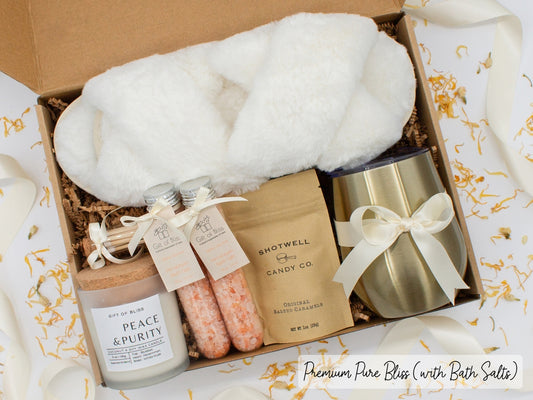Luxury gift box for her. Featuring a stainless steel tumbler, an aromatherapy candle with matches, therapeutic bath salts, plush open-toe slippers, and gourmet caramel treats. All items are beautifully arranged for a pampering experience.