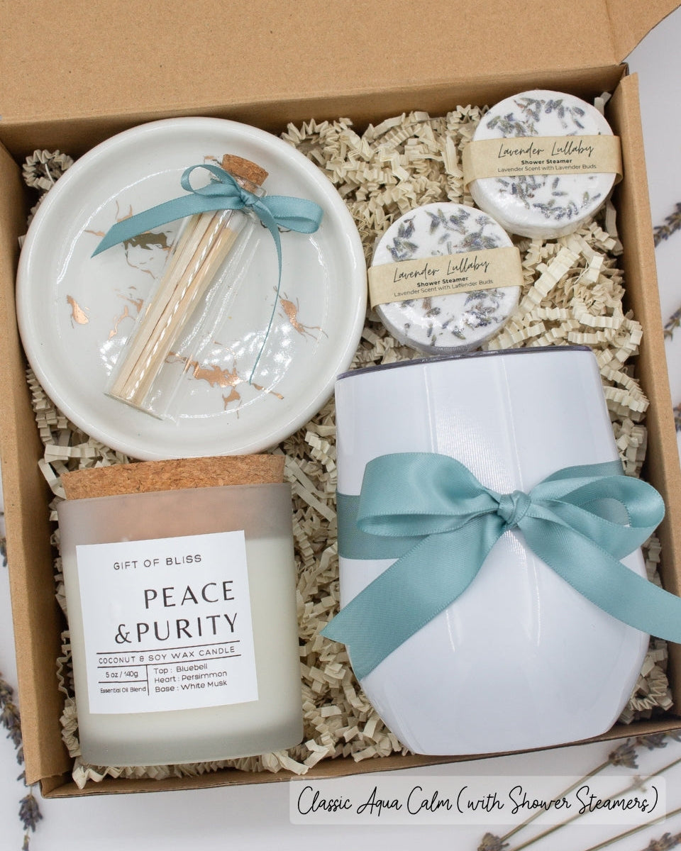 Luxury gift box for her. Featuring a stainless steel tumbler, an aromatherapy candle with matches, aromatic shower steamers, and a sleek ceramic dish. All items are beautifully arranged for a pampering experience.