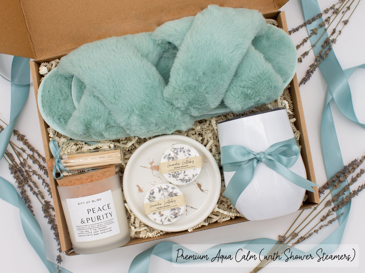 Luxury gift box for her. Featuring a stainless steel tumbler, an aromatherapy candle with matches, aromatic shower steamers, sleek ceramic dish, and plush open-toe slippers. All items are beautifully arranged for a pampering experience.