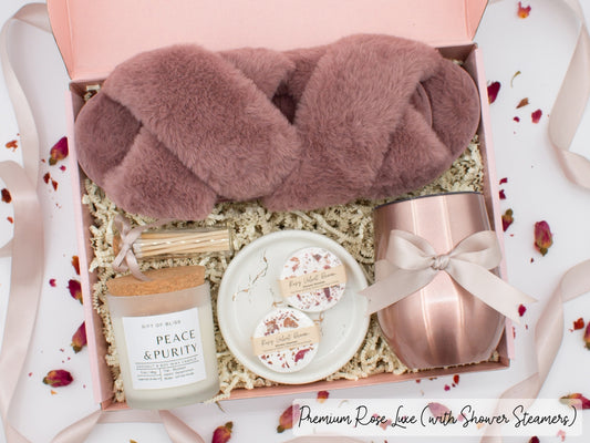Luxury gift box for her. Featuring a stainless steel tumbler, an aromatherapy candle with matches, aromatic shower steamers, sleek ceramic dish, and plush open-toe slippers. All items are beautifully arranged for a pampering experience.