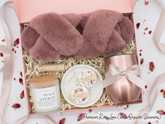 Luxury gift box for her. Featuring a stainless steel tumbler, an aromatherapy candle with matches, aromatic shower steamers, sleek ceramic dish, and plush open-toe slippers. All items are beautifully arranged for a pampering experience.