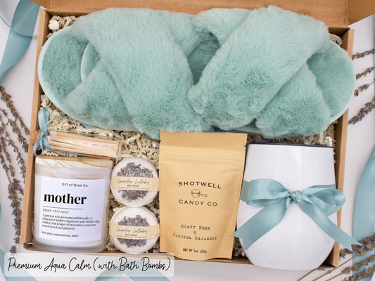 Luxury gift box for mom. Featuring a stainless steel tumbler, an aromatherapy candle with mom-themed label and charming match jar, luxury bath bombs, plush open-toe slippers, and gourmet caramel treats. All items are beautifully arranged for a pampering experience.