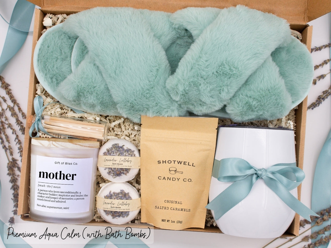 Luxury gift box for mom. Featuring a stainless steel tumbler, an aromatherapy candle with with mom-themed label and charming match jar, luxury bath bombs, plush open-toe slippers, and gourmet caramel treats. All items are beautifully arranged for a pampering experience.