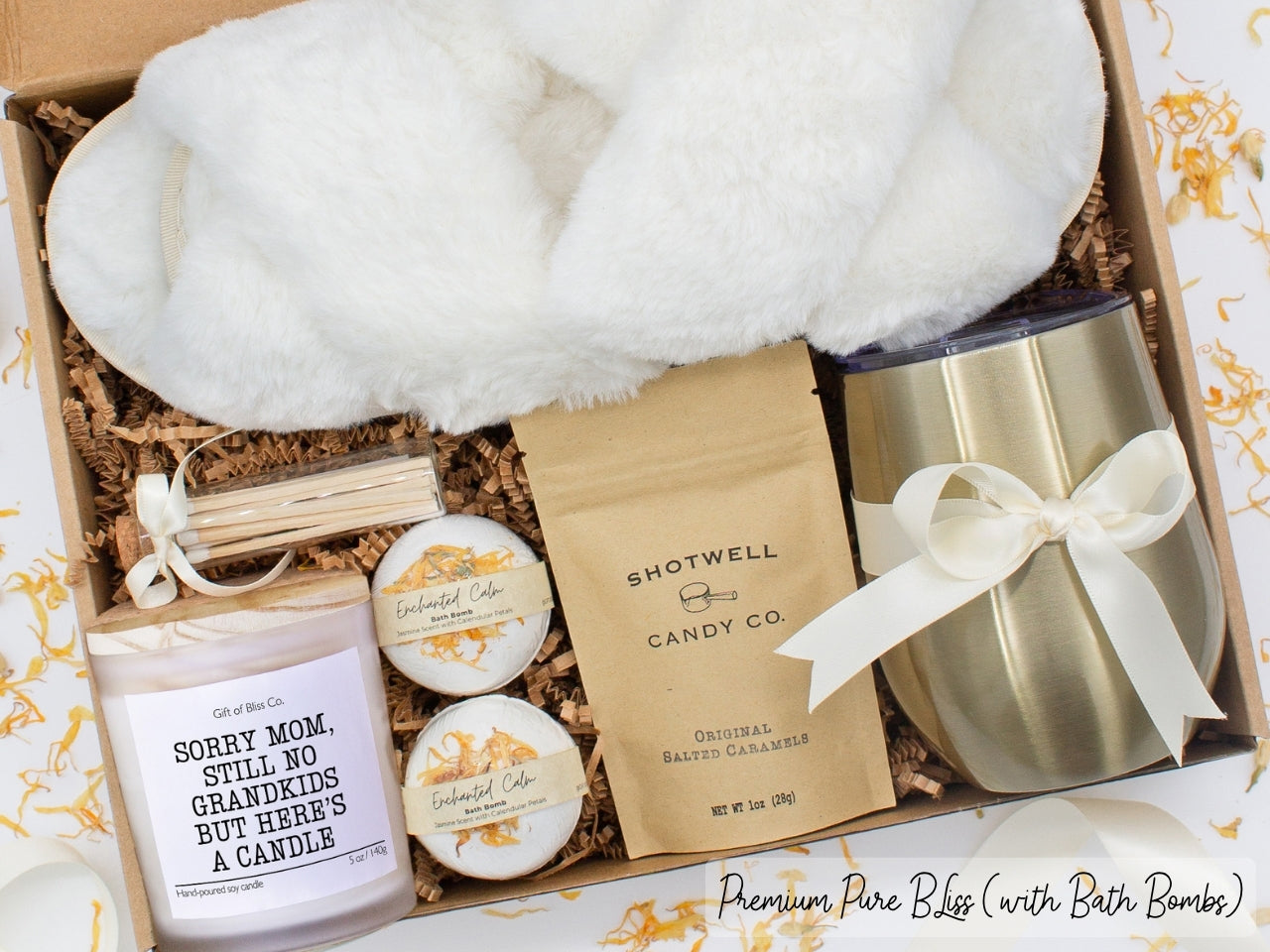 Luxury gift box for mom. Featuring a stainless steel tumbler, an aromatherapy candle with with mom-themed label and charming match jar, luxury bath bombs, plush open-toe slippers, and gourmet caramel treats. All items are beautifully arranged for a pampering experience.