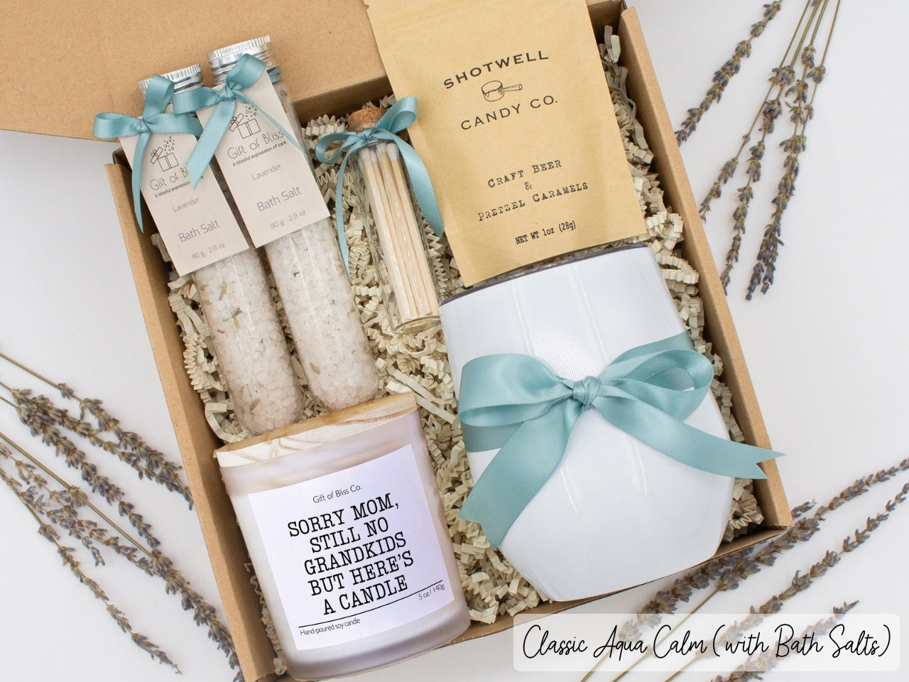 Luxury gift box for her. Featuring a stainless steel tumbler, an aromatherapy candle with mom-themed label and a charming match jar, therapeutic bath salts, and gourmet caramel treats. All items are beautifully arranged for a pampering experience.