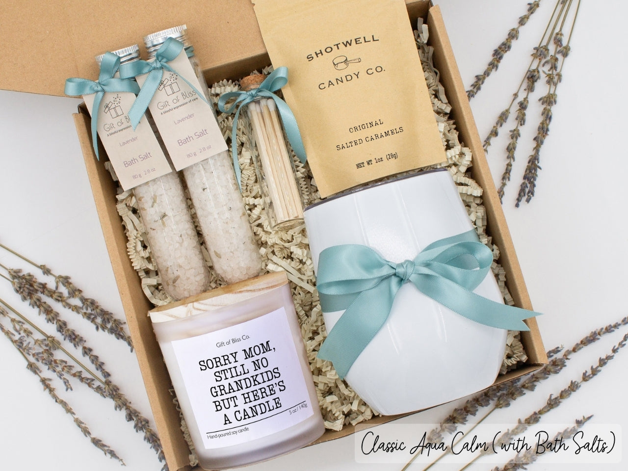 Luxury gift box for mom. Featuring a stainless steel tumbler, an aromatherapy candle with mom-themed label and charming match jar, therapeutic bath salts, and gourmet caramel treats. All items are beautifully arranged for a pampering experience.