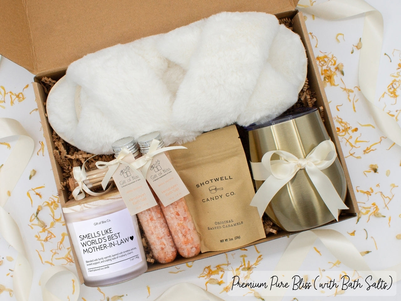 Luxury gift box for mom. Featuring a stainless steel tumbler, an aromatherapy candle with mom-themed label and charming match jar, therapeutic bath salts, plush open-toe slippers, and gourmet caramel treats. All items are beautifully arranged for a pampering experience.