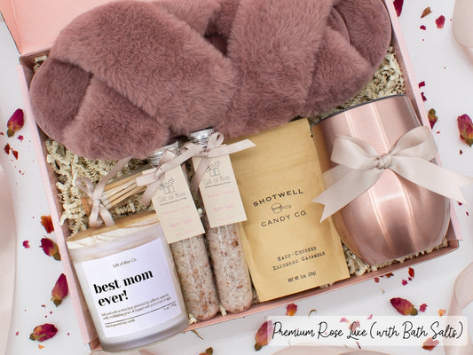 Luxury gift box for her. Featuring a stainless steel tumbler, an aromatherapy candle with mom-themed label and a charming match jar, therapeutic bath salts, plush open-toe slippers, and gourmet caramel treats. All items are beautifully arranged for a pampering experience.