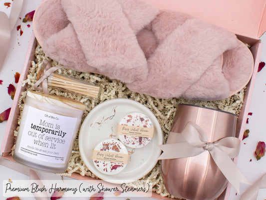Luxury gift box for her. Featuring a stainless steel tumbler, an aromatherapy candle with mom-themed label and charming match jar, aromatic shower steamers, sleek ceramic dish, and plush open-toe slippers. All items are beautifully arranged for a pampering experience.
