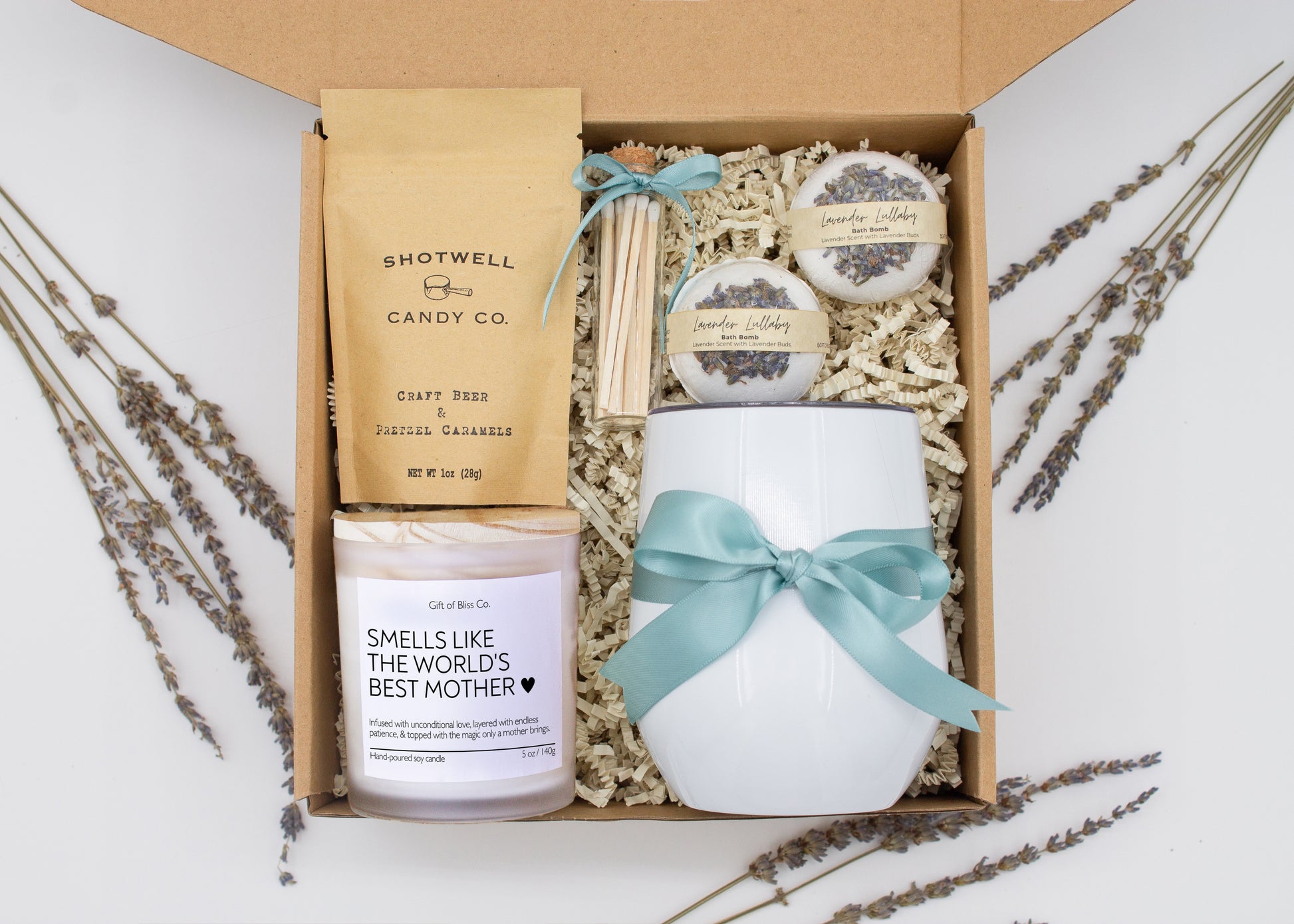 A luxury spa gift box for mom featuring a stainless steel tumbler, an aromatherapy candle with matches, therapeutic bath bombs, and gourmet caramel treats. All items are beautifully arranged for a pampering experience.