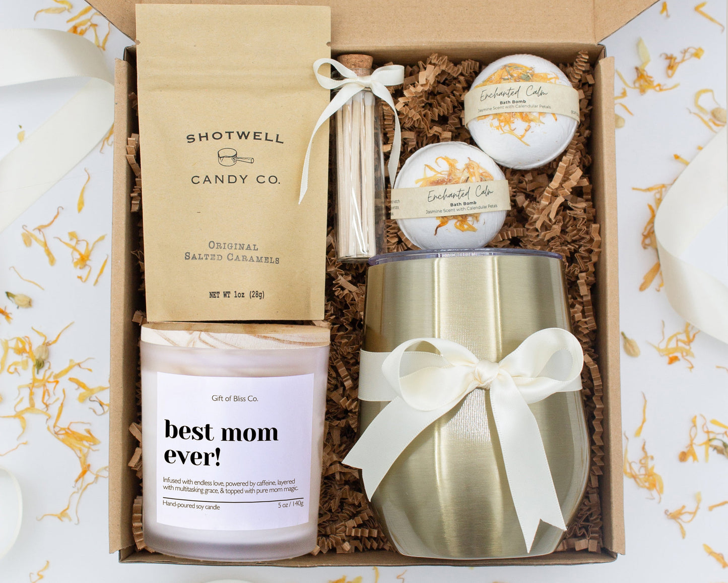 A luxury spa gift box for mom featuring a stainless steel tumbler, an aromatherapy candle with matches, therapeutic bath bombs, and gourmet caramel treats. All items are beautifully arranged for a pampering experience.