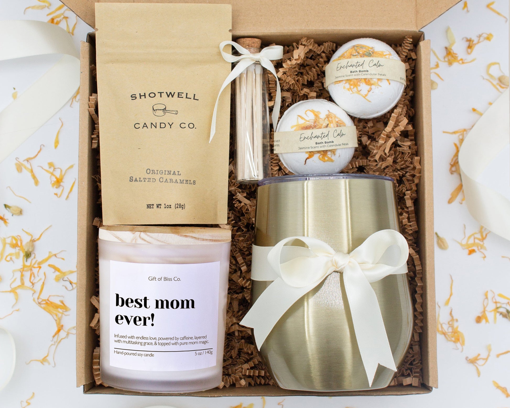 A luxury spa gift box for mom featuring a stainless steel tumbler, an aromatherapy candle with matches, therapeutic bath bombs, and gourmet caramel treats. All items are beautifully arranged for a pampering experience.