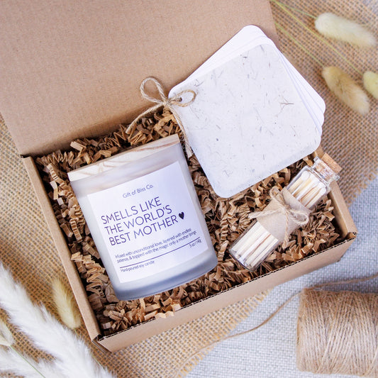 Candle gift box featuring a “Smells Like the World’s Best Mother” soy candle, glass match jar, and a rustic-style personalized message booklet tied with jute twine. Arranged in a kraft box with crinkle paper filler and neutral tones, this cozy, handcrafted gift is perfect for Mother’s Day or mom appreciation. A heartfelt and aesthetic set that combines warmth, functionality, and rustic charm.
