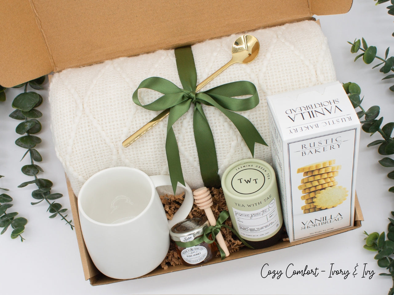 A beautifully arranged gift box for those who love home's warmth and serenity. Includes ceramic mug with golden spoon, tea tube, pure honey with wooden dipper, buttery shortbread, and soft knit blanket, all ensuring a cozy, comforting experience.