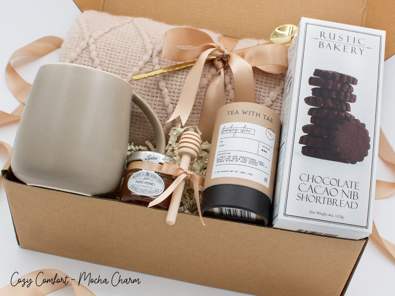 A beautifully arranged gift box for those who love home's warmth and serenity. Includes ceramic mug with golden spoon, tea tube, pure honey with wooden dipper, buttery shortbread, and soft knit blanket, all ensuring a cozy, comforting experience.