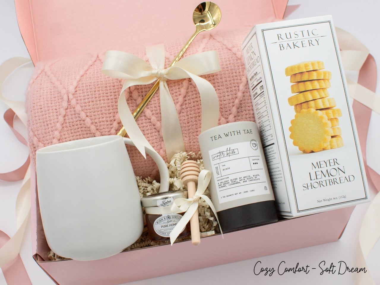 A beautifully arranged gift box for those who love home's warmth and serenity. Includes ceramic mug with golden spoon, tea tube, pure honey with wooden dipper, buttery shortbread, and soft knit blanket, all ensuring a cozy, comforting experience.