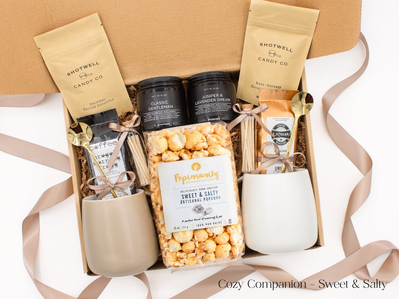 A gift box for two. Includes two ceramic mugs with golden spoons, a selection of fine coffees, two safety match jars, his and hers aromatherapy candles, caramel candies, and artisan popcorn, all for shared moments of joy.