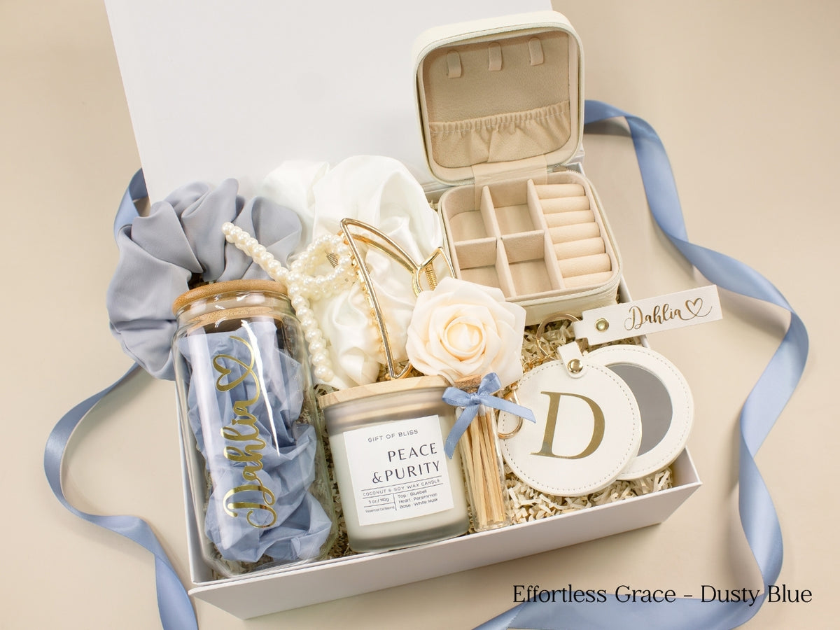 Dusty blue gift box for her featuring personalized glass tumbler, open jewelry case, candle, satin scrunchies, pearl hair accessories, gold claw clip and mirror.