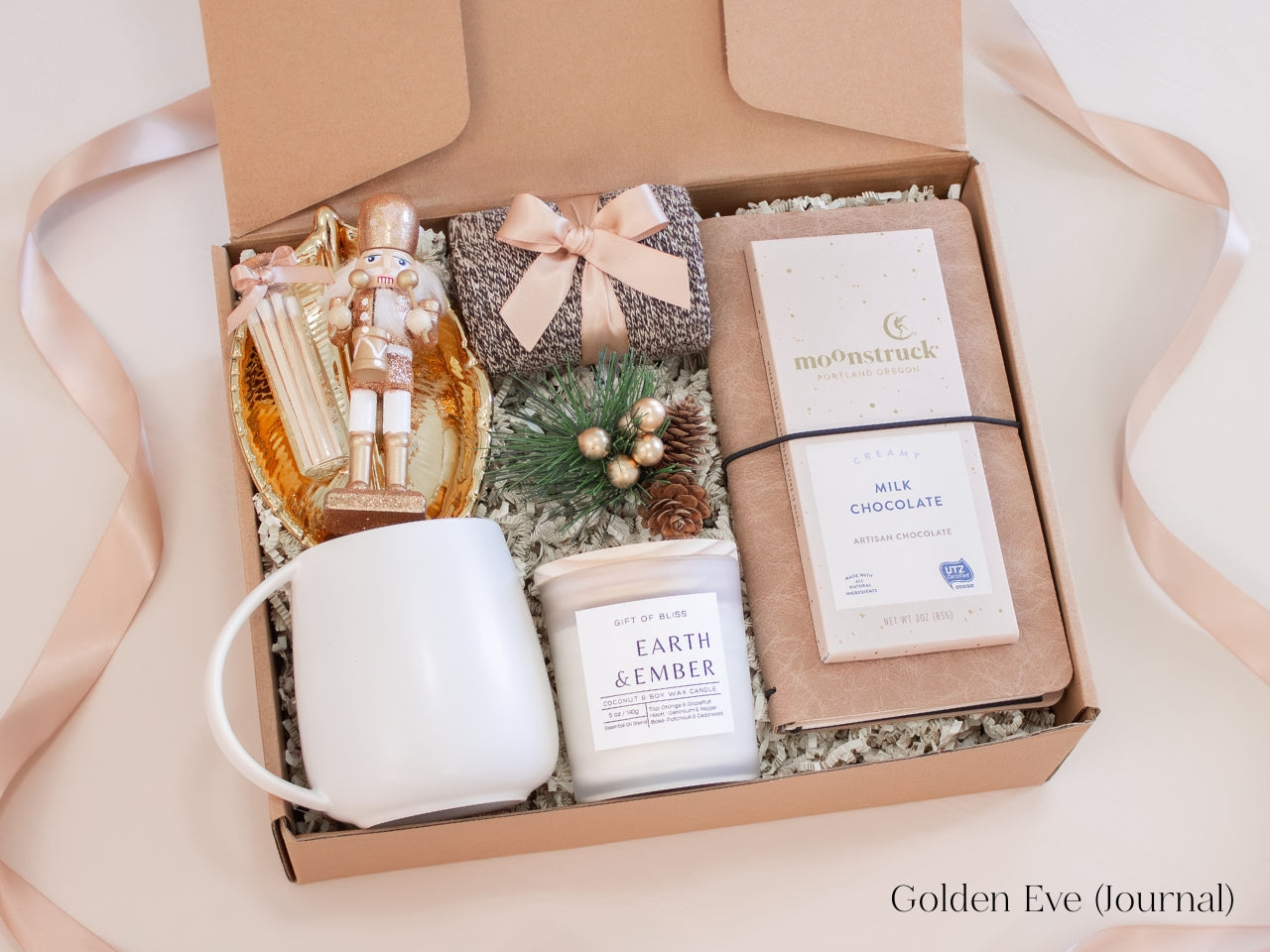 Stylish holiday gift box for him in champagne and gold tones including a white ceramic mug with gold spoon, Earth & Ember candle, artisan milk chocolate bar, journal, nutcracker figurine, and gold leaf catchall dish - a sophisticated Christmas gift with a warm, elegant feel.