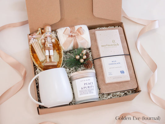 Stylish holiday gift box for him in champagne and gold tones including a white ceramic mug with gold spoon, Earth & Ember candle, artisan milk chocolate bar, journal, nutcracker figurine, and gold leaf catchall dish - a sophisticated Christmas gift with a warm, elegant feel.
