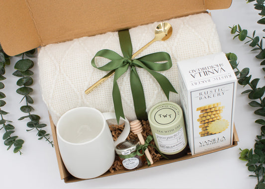 A beautifully arranged gift box for those who love home's warmth and serenity. Includes ceramic mug with golden spoon, tea tube, pure honey with wooden dipper, buttery shortbread, and soft knit blanket, all ensuring a cozy, comforting experience.