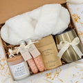 Luxury gift box for her. Featuring a stainless steel tumbler, an aromatherapy candle with matches, therapeutic bath salt, plush open-toe slippers, and gourmet caramel treats. All items are beautifully arranged for a pampering experience.