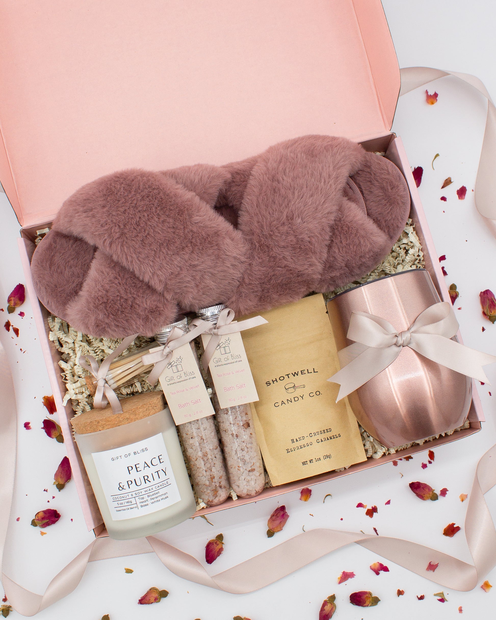 Luxury gift box for her. Featuring a stainless steel tumbler, an aromatherapy candle with matches, therapeutic bath salt, plush open-toe slippers, and gourmet caramel treats. All items are beautifully arranged for a pampering experience.