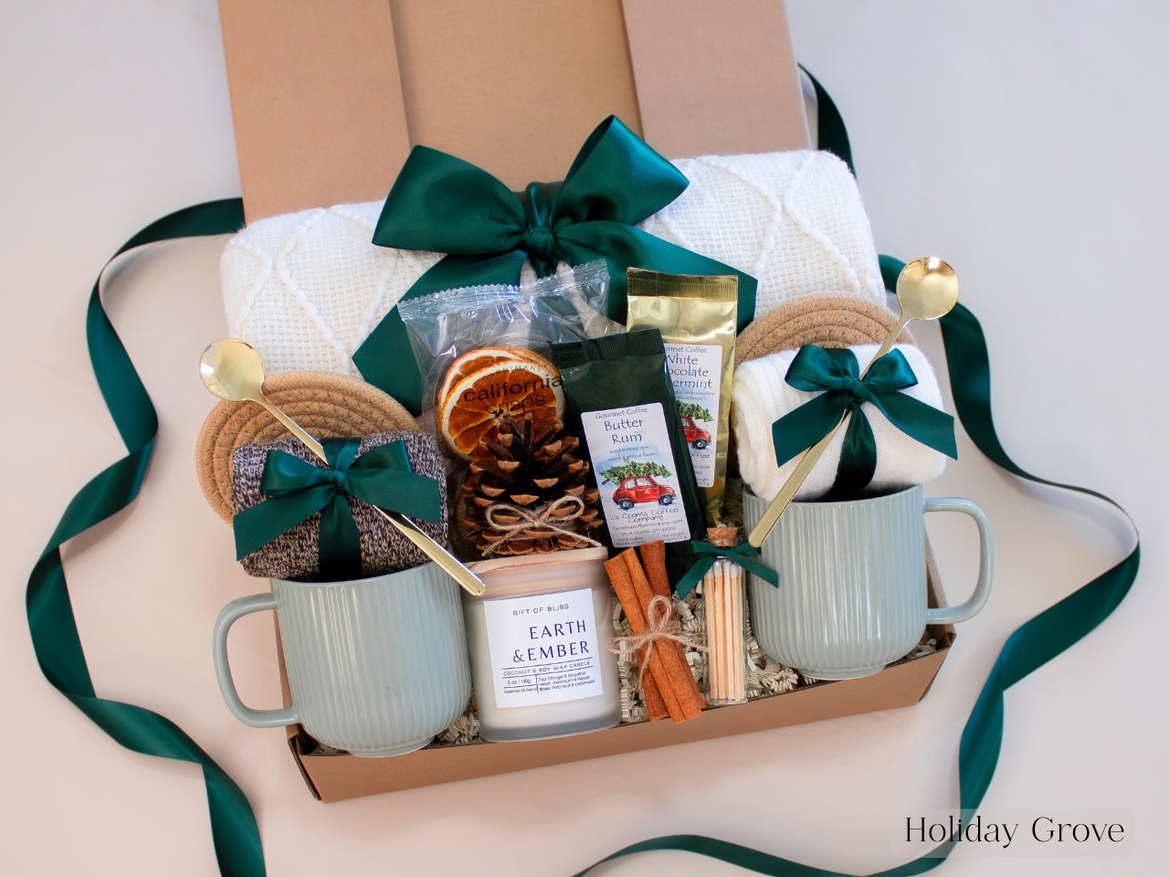Rustic winter gift box in spruce green with ceramic mugs, cinnamon sticks, dried oranges, pinecones, and seasonal coffee — a festive and earthy holiday gift set for couples.
